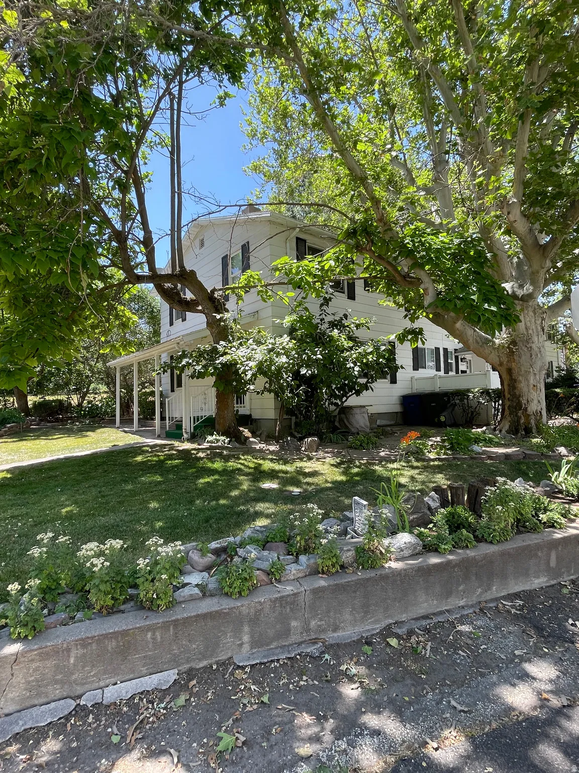 Two-story home with white siding and dark shutters, featuring a wraparound porch with white railings Yard