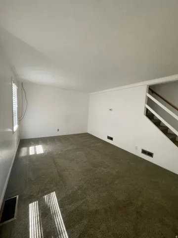 Spacious room featuring neutral carpeting, white walls, and a staircase with open risers