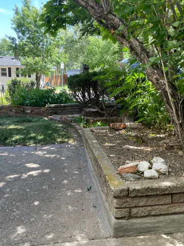 Front yard featuring mature trees, concrete paving, and a brick retaining wall