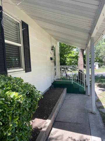 Covered front porch featuring white siding, black louvered shutters, and a concrete walkway