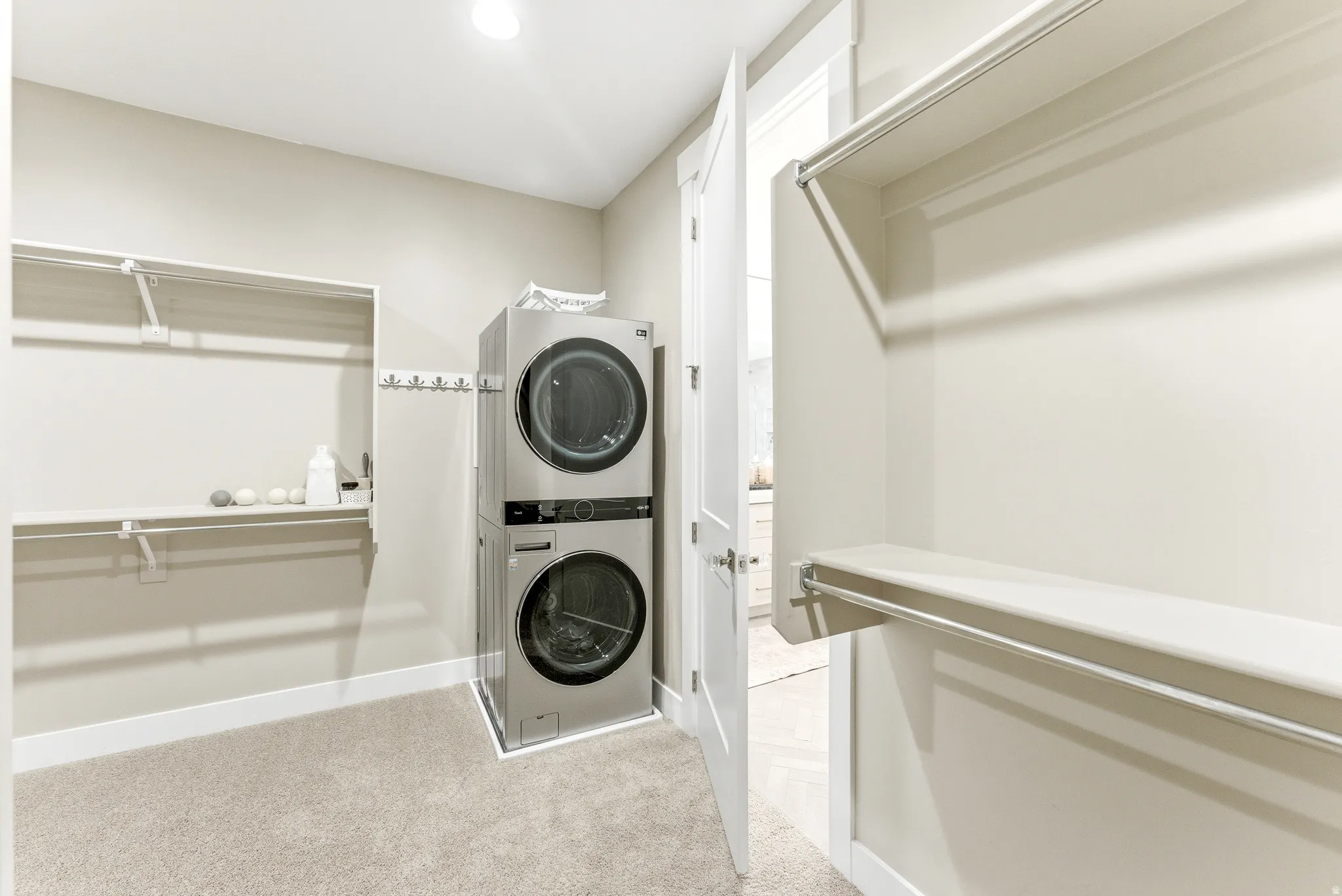 Dedicated laundry area featuring a stacked washer and dryer unit, integrated shelving, hanging rods, and light-toned carpeting