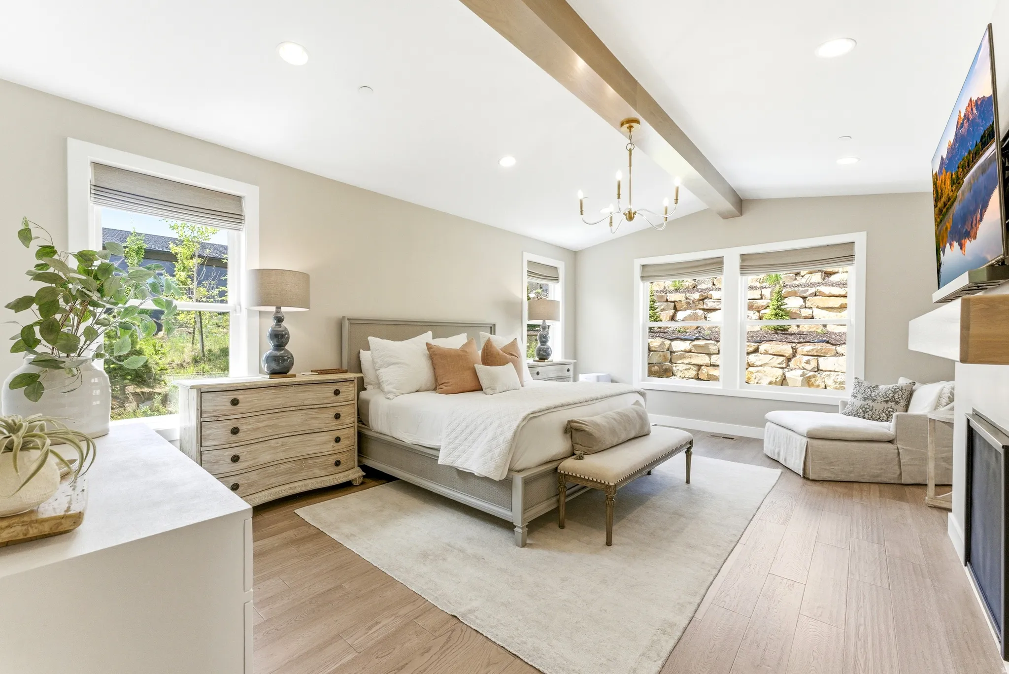 Spacious room featuring vaulted ceilings with exposed wood-finish beams, a modern chandelier, and light wood-finish flooring