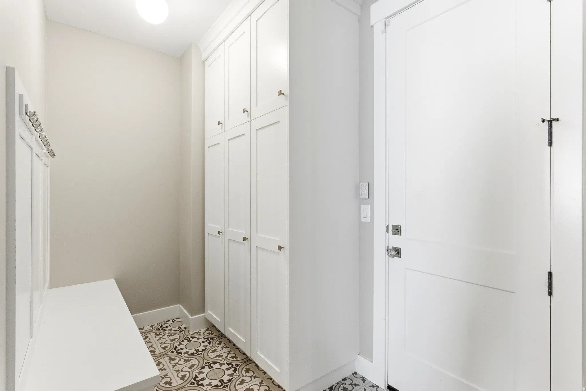 Entryway featuring patterned tile flooring, built-in storage cabinetry with gold-tone hardware, and a white built-in bench with coat hooks