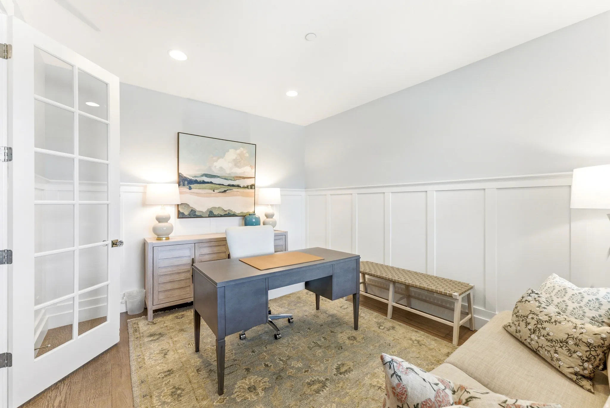French doors with glass lites, wood-finish flooring, recessed ceiling lighting, and wainscoting details characterize this interior space