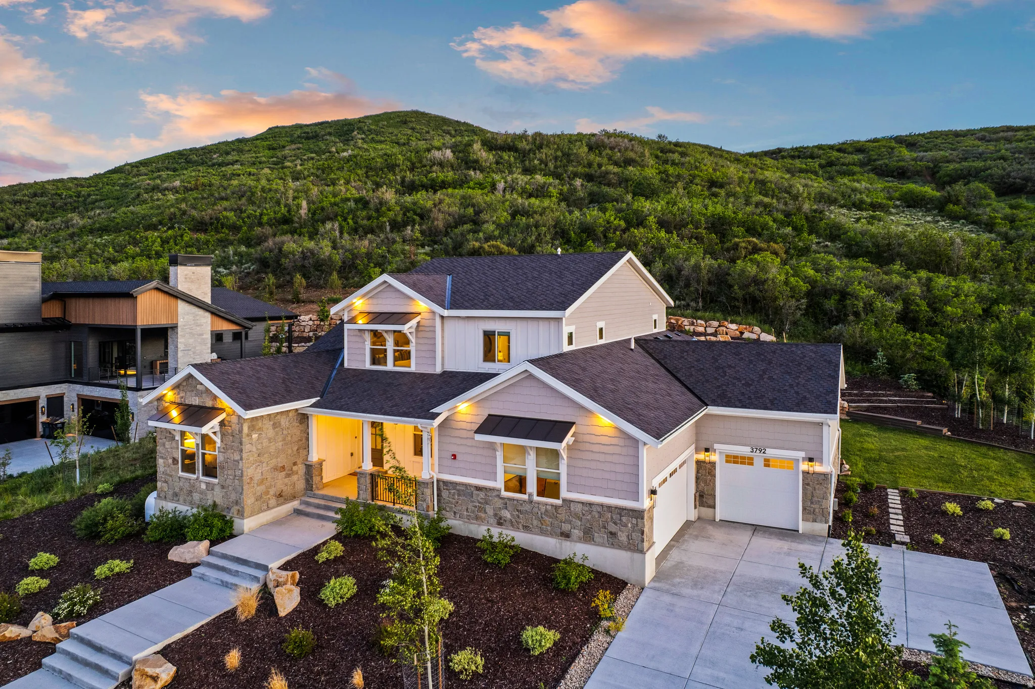 Contemporary residence featuring stone and siding exterior, a multi-car driveway, attached two-car garage, and tiered landscaping
