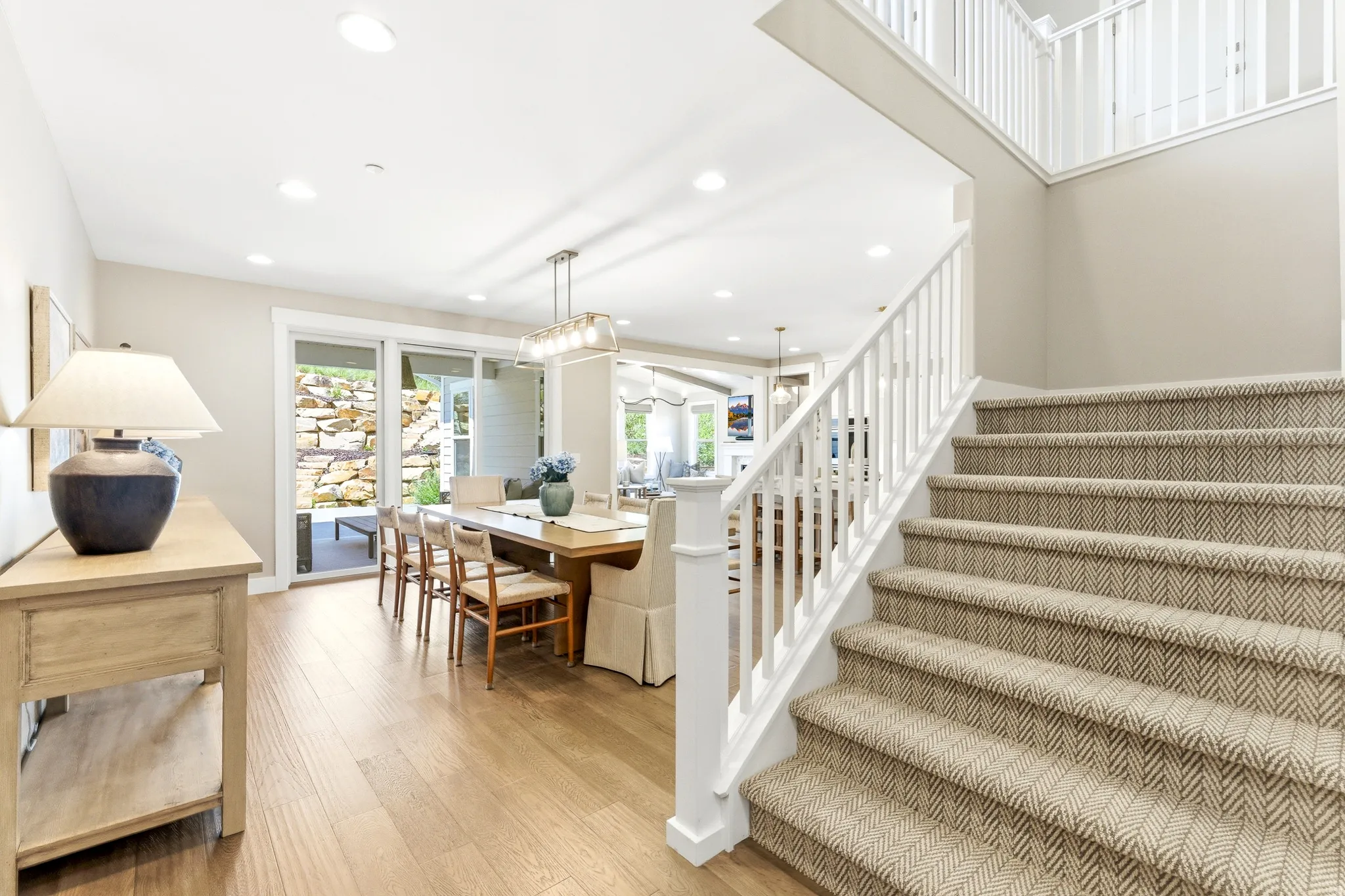 Two-story entryway featuring wood-finish flooring, a carpeted staircase with white balusters, recessed lighting, and a dining area with sliding glass doors