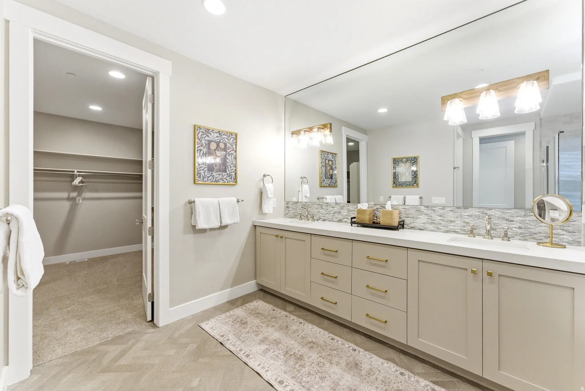 Dual vanity with light cabinetry, gold-toned hardware, solid surface countertops, and a full-width mirror