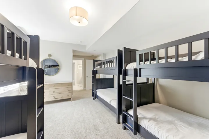 Spacious room featuring multiple dark-stained bunk beds, light-colored carpeting, and a ceiling-mounted drum light fixture