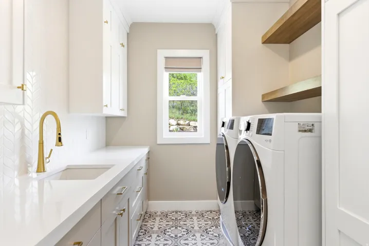 Functional utility room featuring a large undermount sink with a brass-finish faucet, extensive countertop space, and patterned floor tile