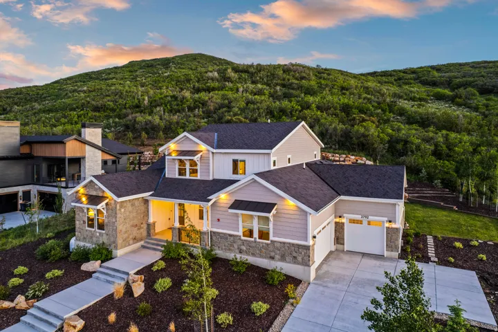 Contemporary residence featuring stone and siding exterior, a multi-car driveway, attached two-car garage, and tiered landscaping