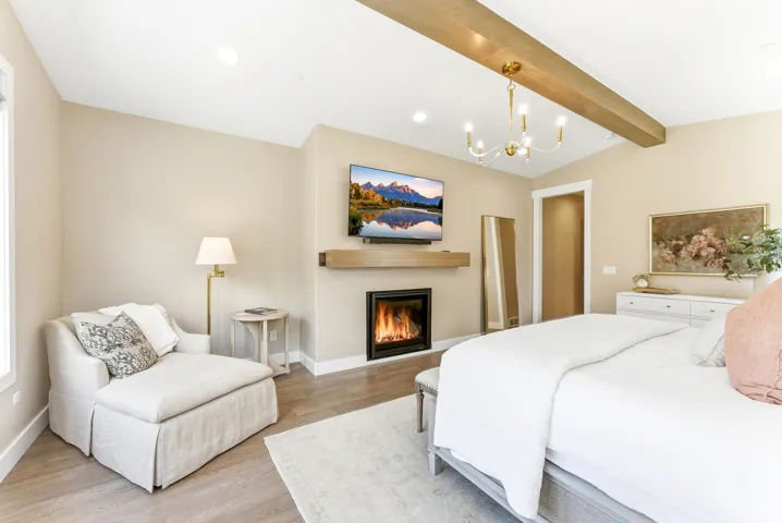 Spacious bedroom featuring vaulted ceilings with exposed wood beams, a built-in fireplace with a wood-finish mantel, and light wood-finish flooring
