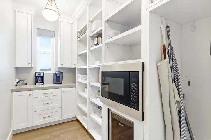 Bright utility space featuring white cabinetry, a built-in microwave, a beverage cooler, and extensive shelving