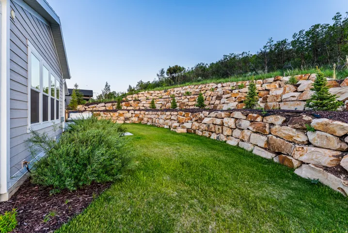 Expansive terraced rock wall landscaping featuring young evergreen trees and integrated mulch beds