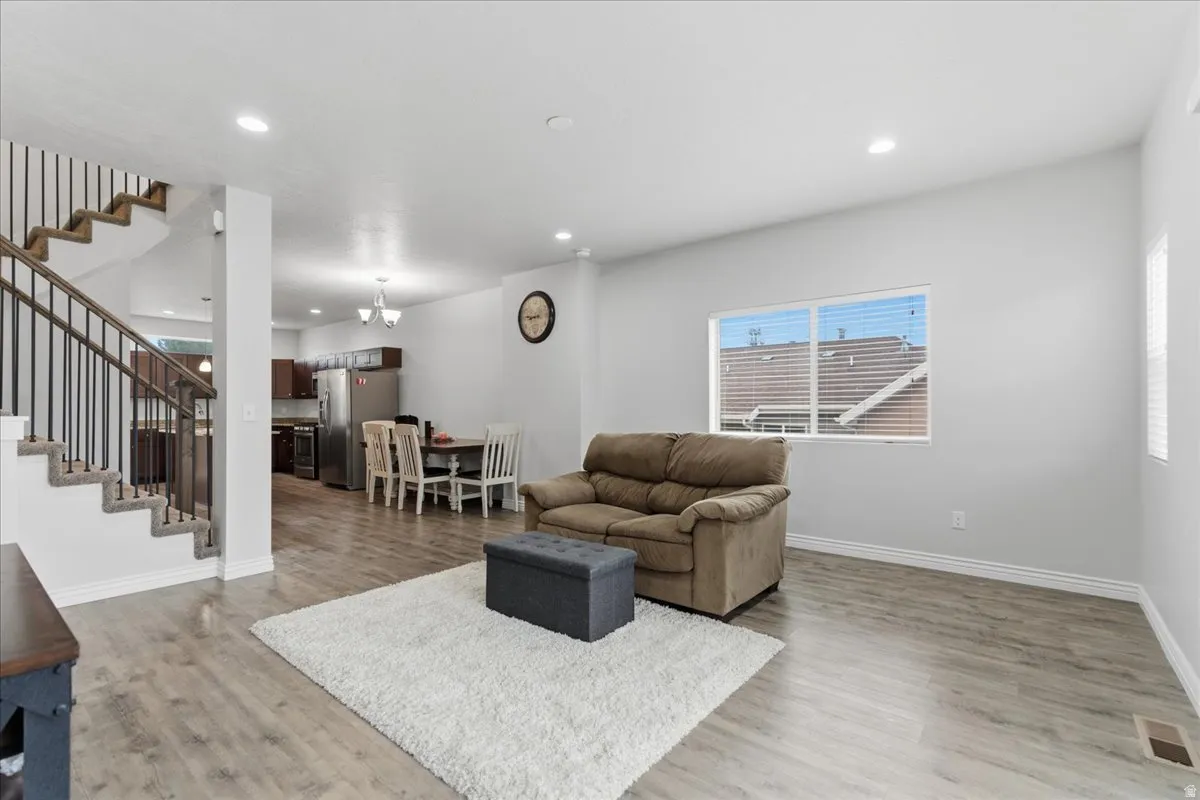 Open-concept living area featuring wood-finish flooring, recessed lighting, and a prominent staircase with metal balusters