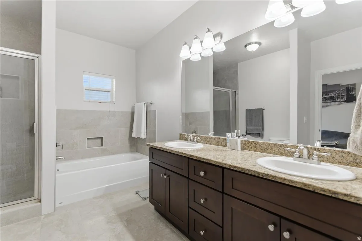 Bathroom featuring a dual vanity with granite-style countertops, wood-finish cabinetry, and undermount sinks