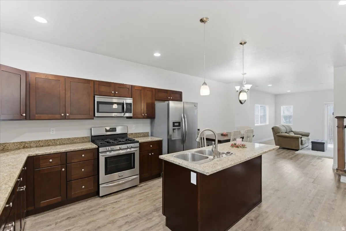 Open-concept kitchen featuring dark wood cabinetry, stainless steel appliances, speckled countertops, and a central island with a double basin sink