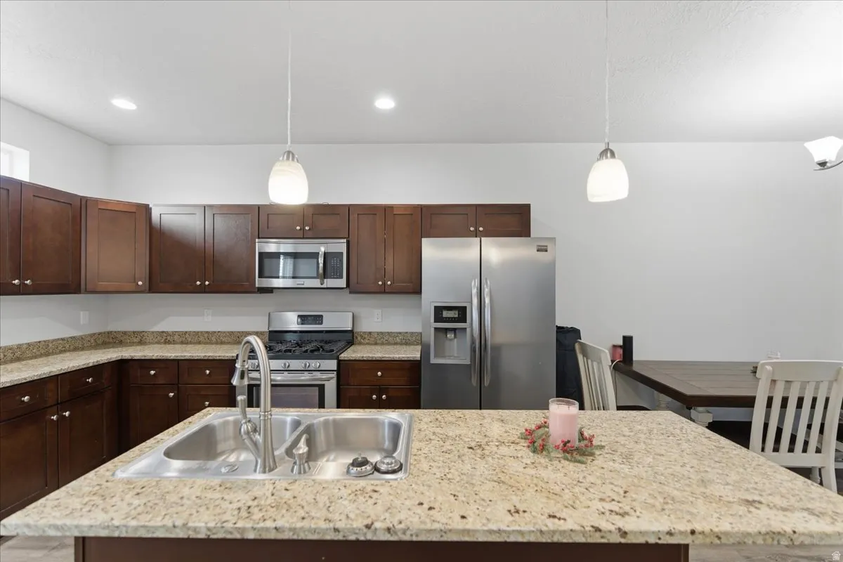 Spacious kitchen featuring an island with a double stainless steel sink, granite countertops, and rich wood cabinetry