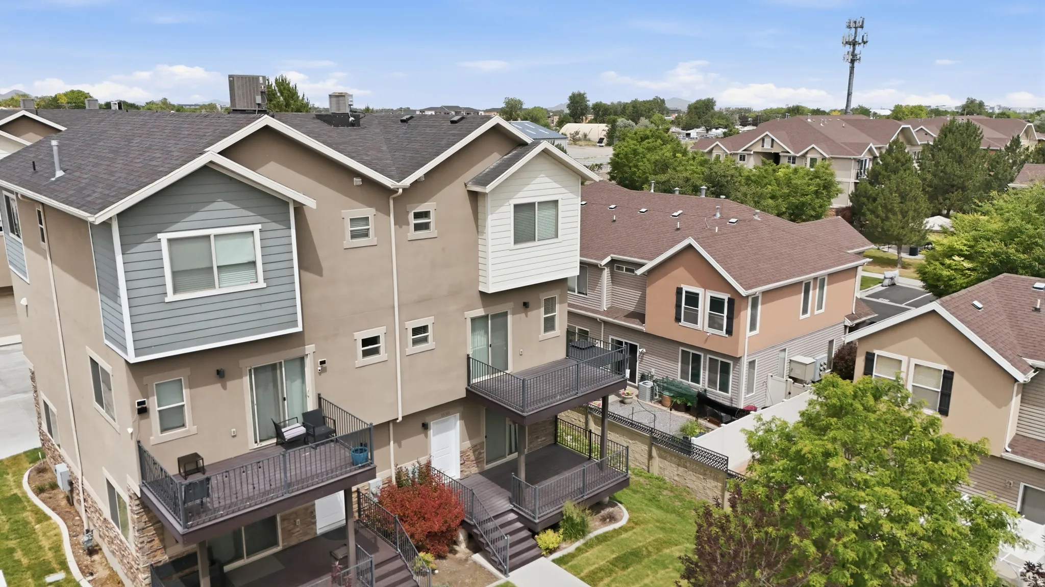 Multi-level townhome exterior featuring an upper balcony, lower patio, and stairs leading to a landscaped yard