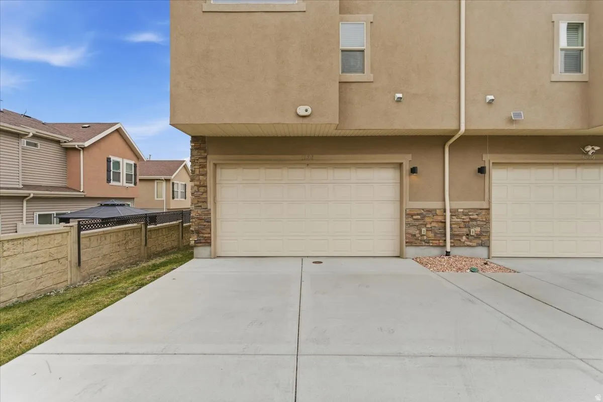 Stucco exterior with stacked stone accents, featuring a concrete driveway and an attached garage with a panel door