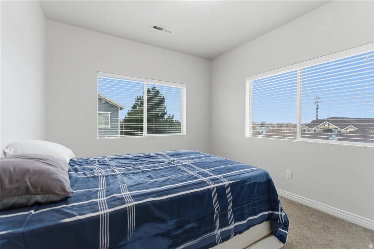 Bedroom featuring two large windows with horizontal blinds, light gray wall paint, and gray carpet flooring