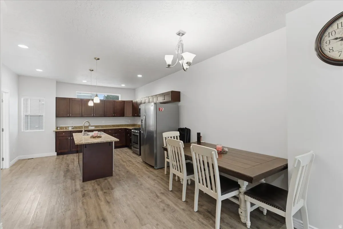 Open-concept kitchen and dining area featuring wood-finish flooring, dark wood cabinetry, a center island with a stone countertop, recessed lighting, and stainless steel appliances