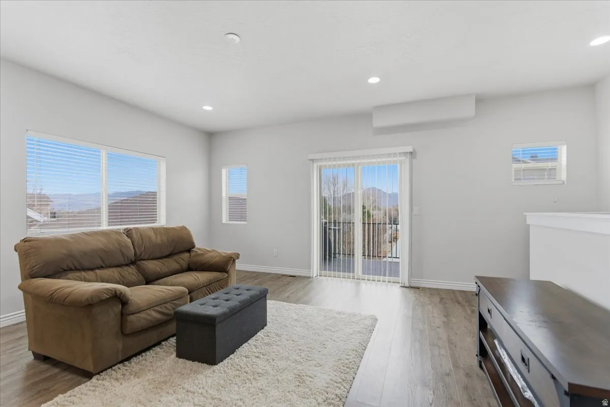 Spacious living area featuring expansive windows, wood-finish flooring, recessed lighting, and a sliding glass door opening to a balcony