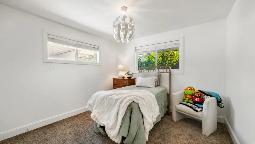 Second bedroom featuring two windows with white blinds, a contemporary ceiling light fixture, and neutral carpeting