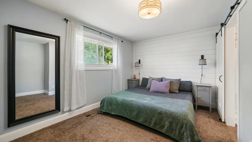 Primary bedroom featuring shiplap accent wall, flush-mount ceiling light, window with white blinds, and carpeted flooring