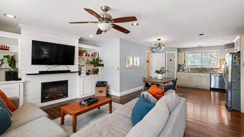 Open-concept living space featuring wood-finish flooring, a contemporary fireplace with shiplap surround, and built-in shelving