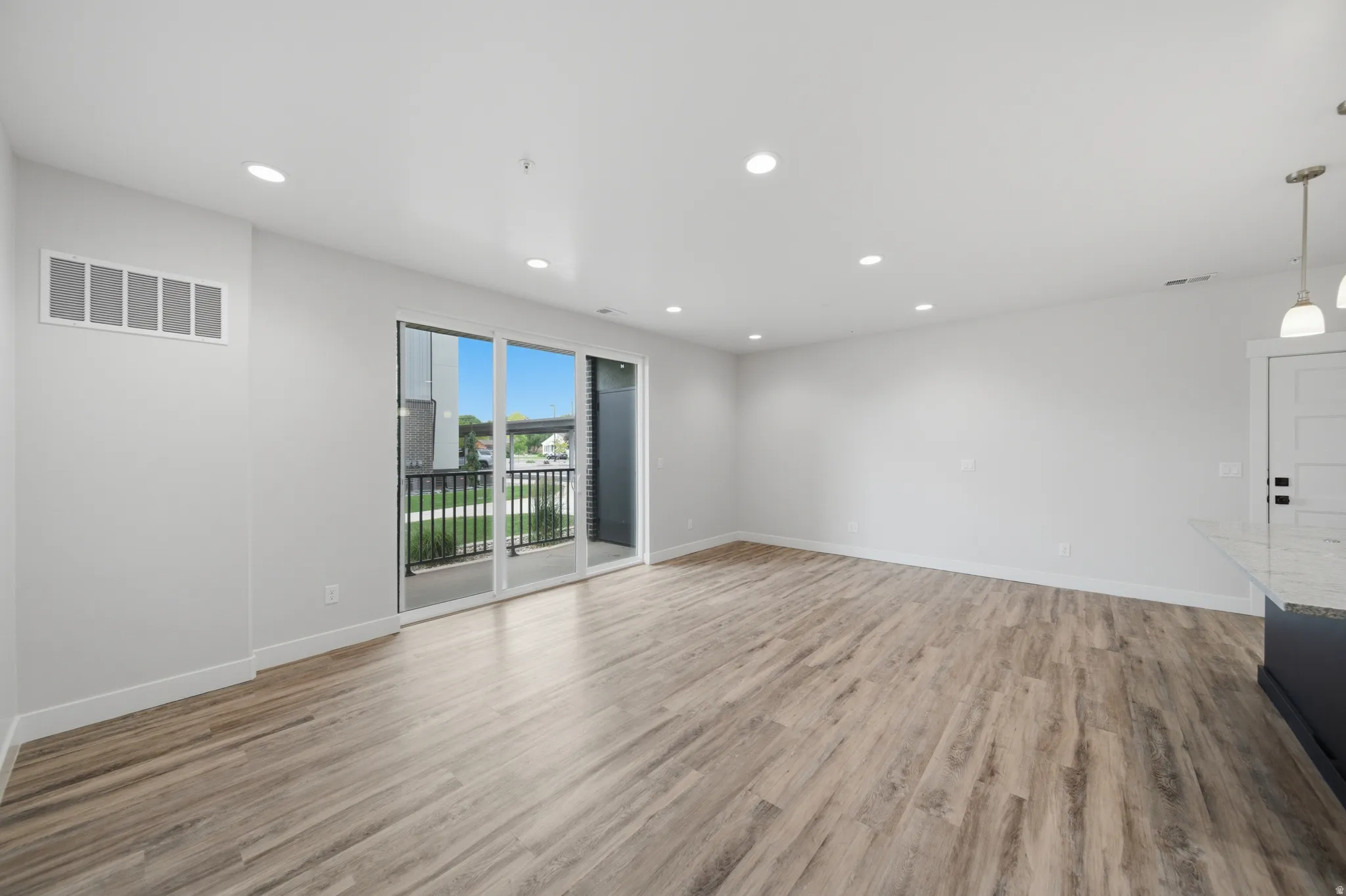 Spacious interior featuring wood-finish flooring, recessed lighting, and a sliding glass door opening to a private balcony with black railings
