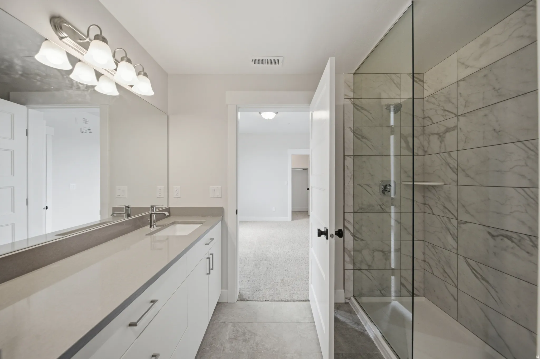 Bathroom featuring an extended vanity with an undermount sink, a large mirror, and a glass-enclosed shower with tiled walls