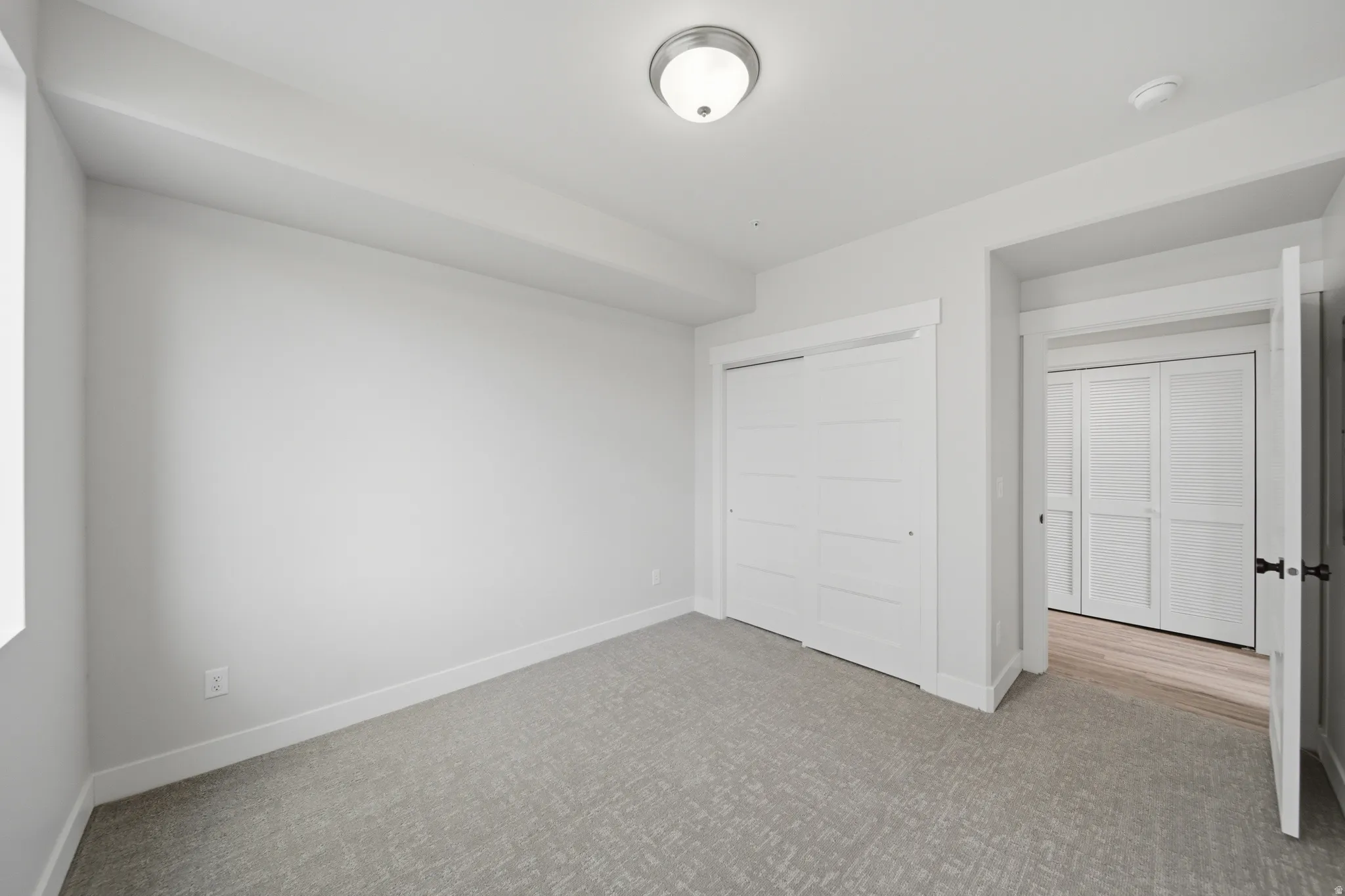 Carpeted room featuring a window, built-in sliding closet doors, and a ceiling-mounted light fixture