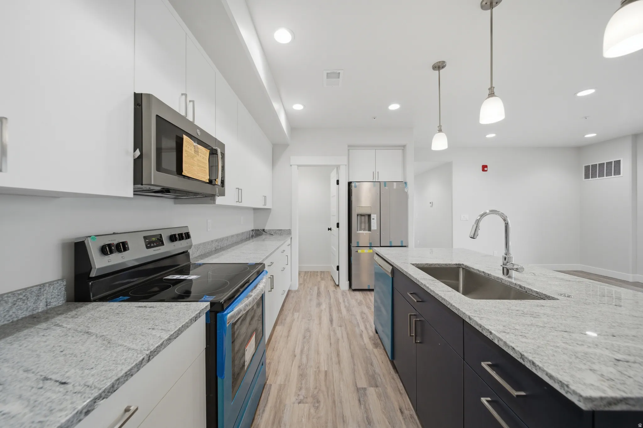 Modern kitchen with light wood-finish flooring, white upper cabinetry, and contrasting dark lower island cabinetry