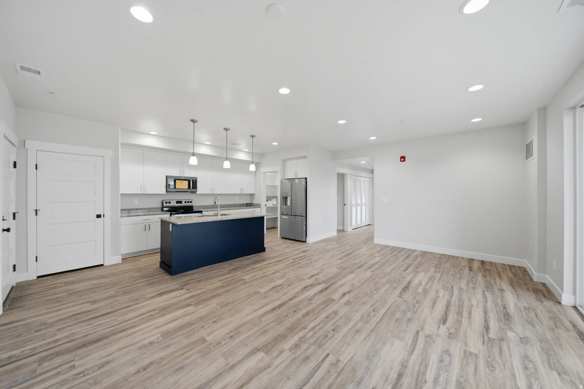 Open-concept living area featuring wood-finish flooring, a contemporary kitchen with white cabinetry, stainless steel appliances, a central island with a contrasting navy base, and recessed lighting