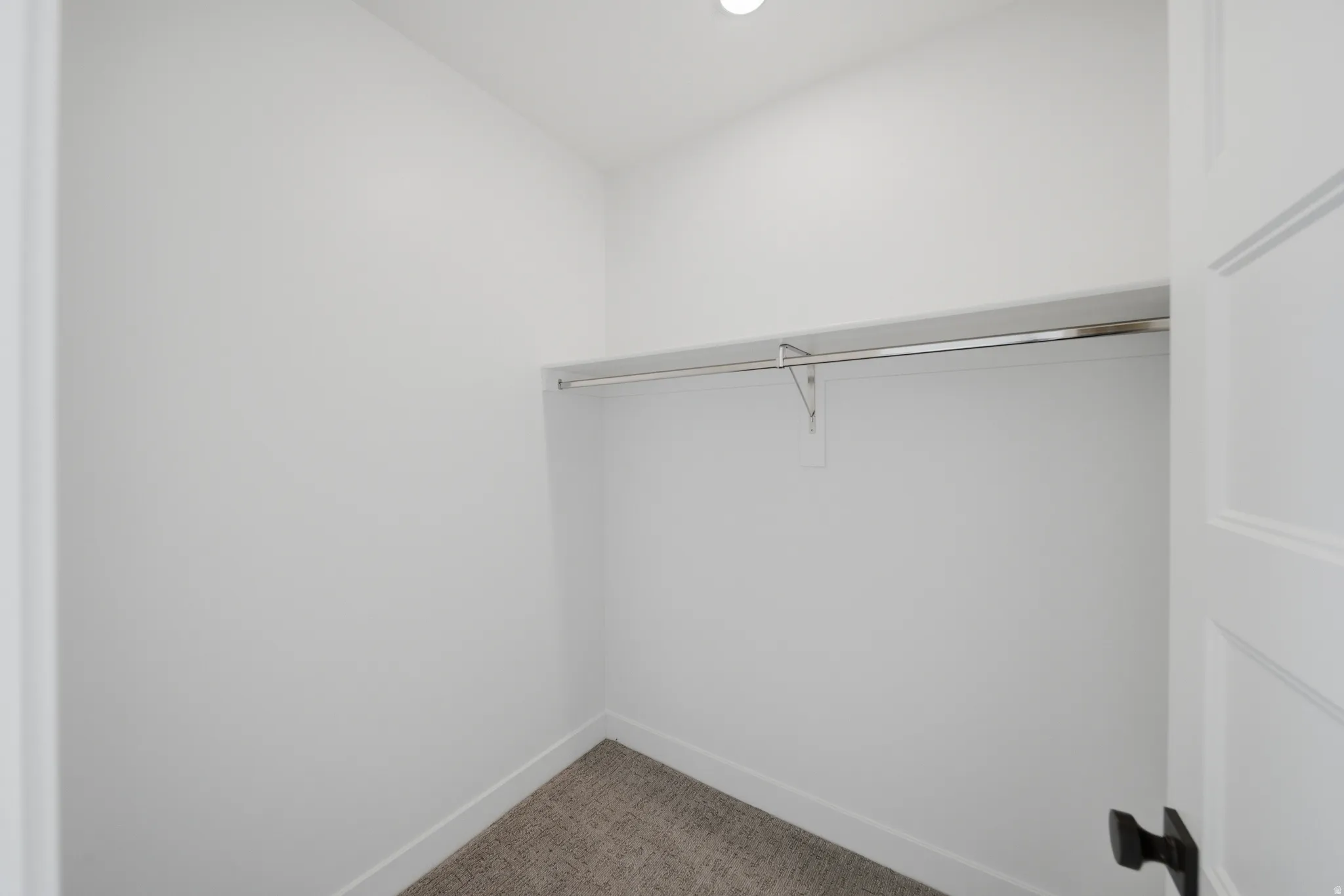 Recessed lighting illuminates this closet, featuring a single hanging rod, upper shelving, and carpet flooring