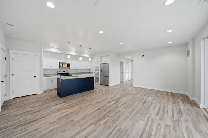 Open-concept living area featuring wood-finish flooring, a contemporary kitchen with white cabinetry, stainless steel appliances, a central island with a contrasting navy base, and recessed lighting