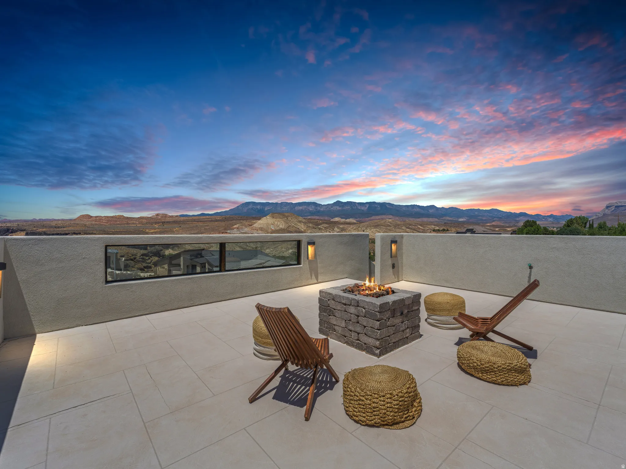 Expansive rooftop patio featuring a stone fire pit, built-in lighting, a low privacy wall, and panoramic mountain scenery