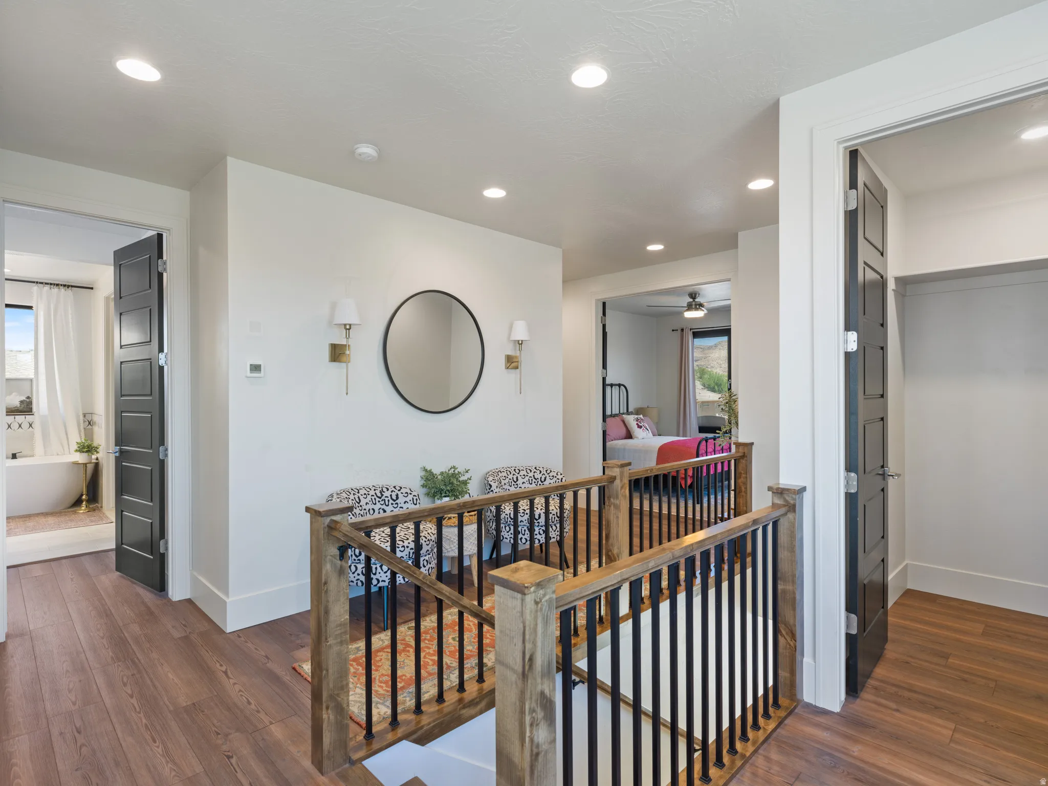 Upper-level hallway featuring  a wood and wrought iron staircase railing, recessed lighting, and modern black interior doors