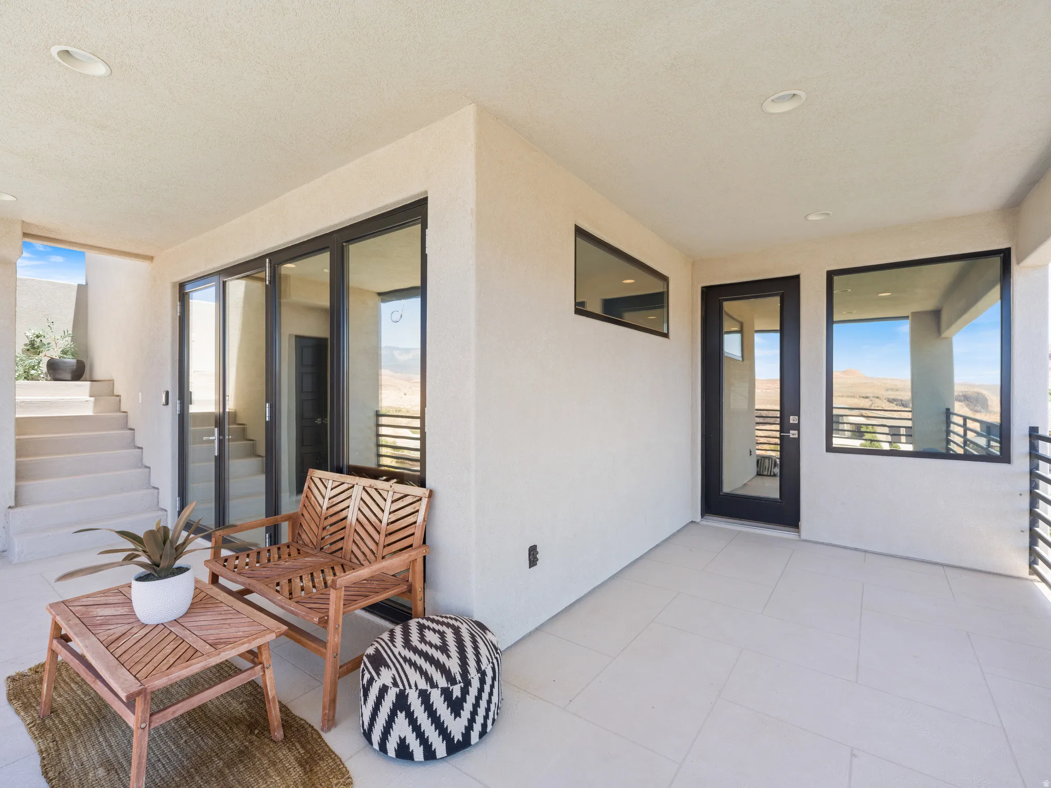 Covered outdoor patio featuring  multiple large black-framed glass sliding doors, and a transparent glass entry door to the upstairs hallway