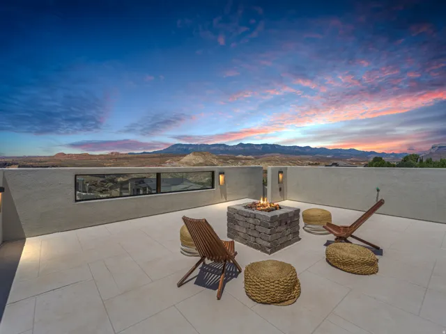 Expansive rooftop patio featuring a stone fire pit, built-in lighting, a low privacy wall, and panoramic mountain scenery