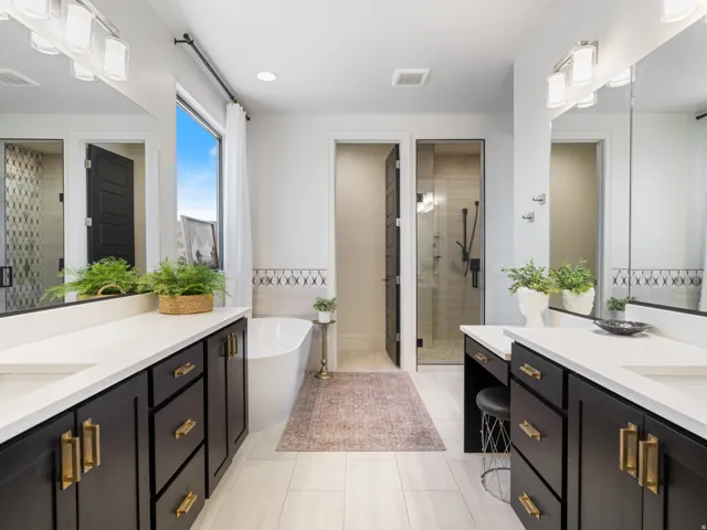 Modern bathroom featuring dual vanities with dark cabinetry and gold-tone hardware a walk in shower with dual shower heads