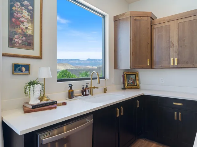 Kitchen area featuring a built-in stainless steel dishwasher, white countertop, and a white integrated sink with a gold-finish faucet