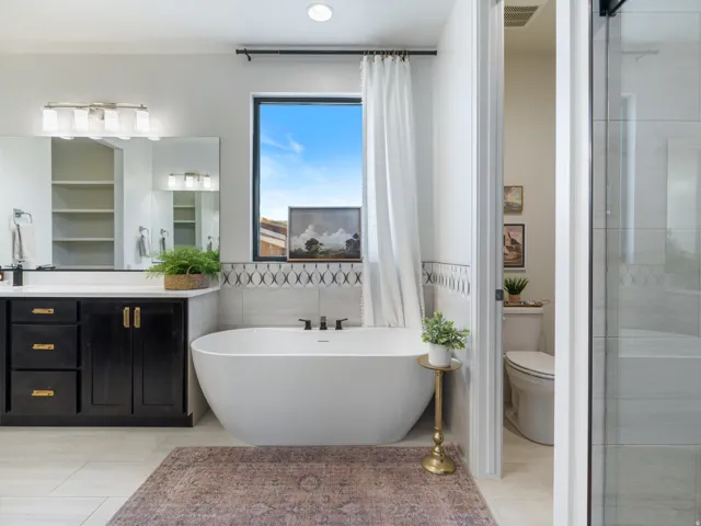 Bathroom featuring a freestanding soaking tub, a black vanity with a white countertop and gold hardware, a large mirror, and tiled flooring