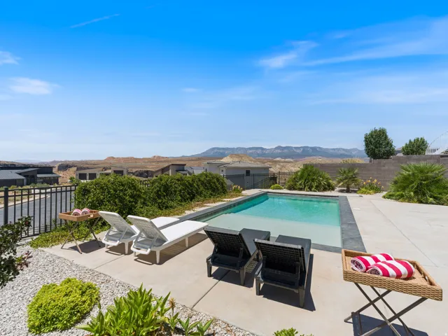 Rear patio featuring a rectangular swimming pool with a dark coping, large tanning deck in the pool surrounded by concrete decking and xeriscaping