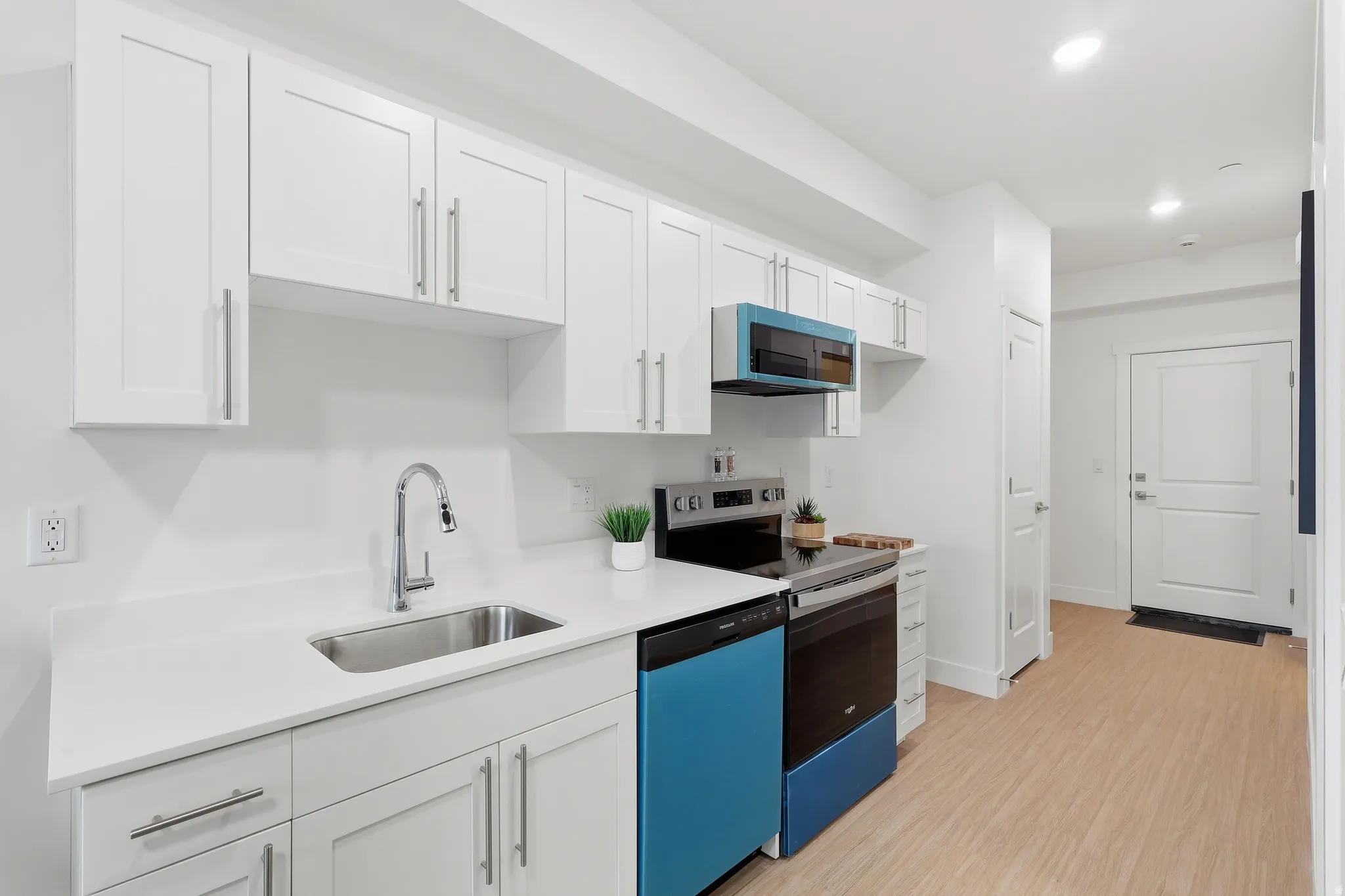 Modern kitchen featuring white shaker cabinetry, stainless steel sink, light-toned countertops, and light wood-finish flooring