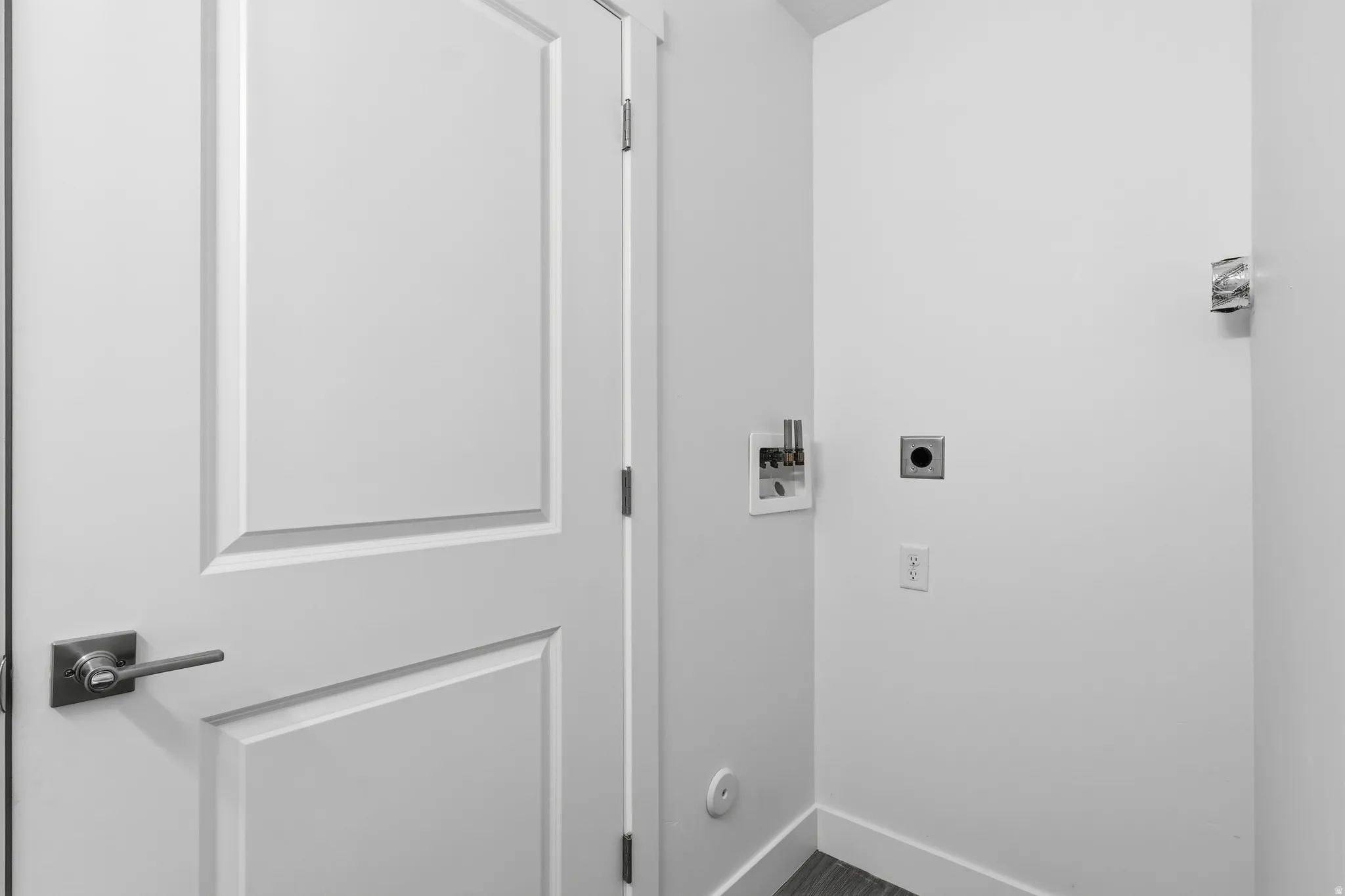 Utility area featuring a paneled door with brushed nickel hardware, a white laundry hookup box, a dryer vent, and electrical outlets