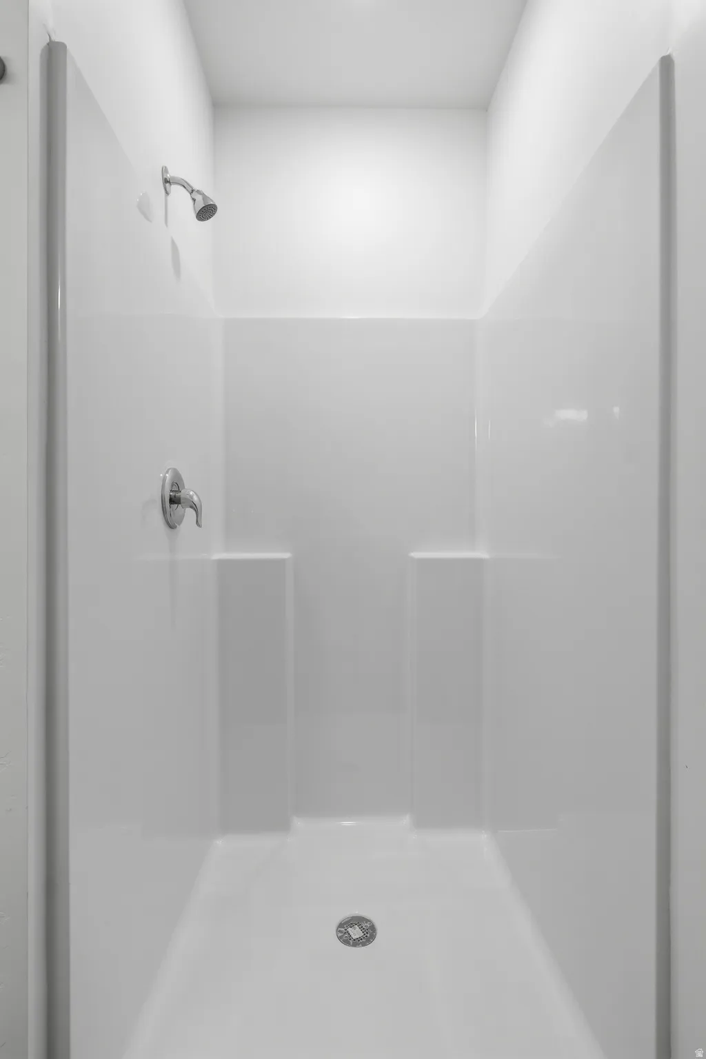 White shower enclosure with integrated shelving, chrome fixtures, and a ceiling-mounted showerhead