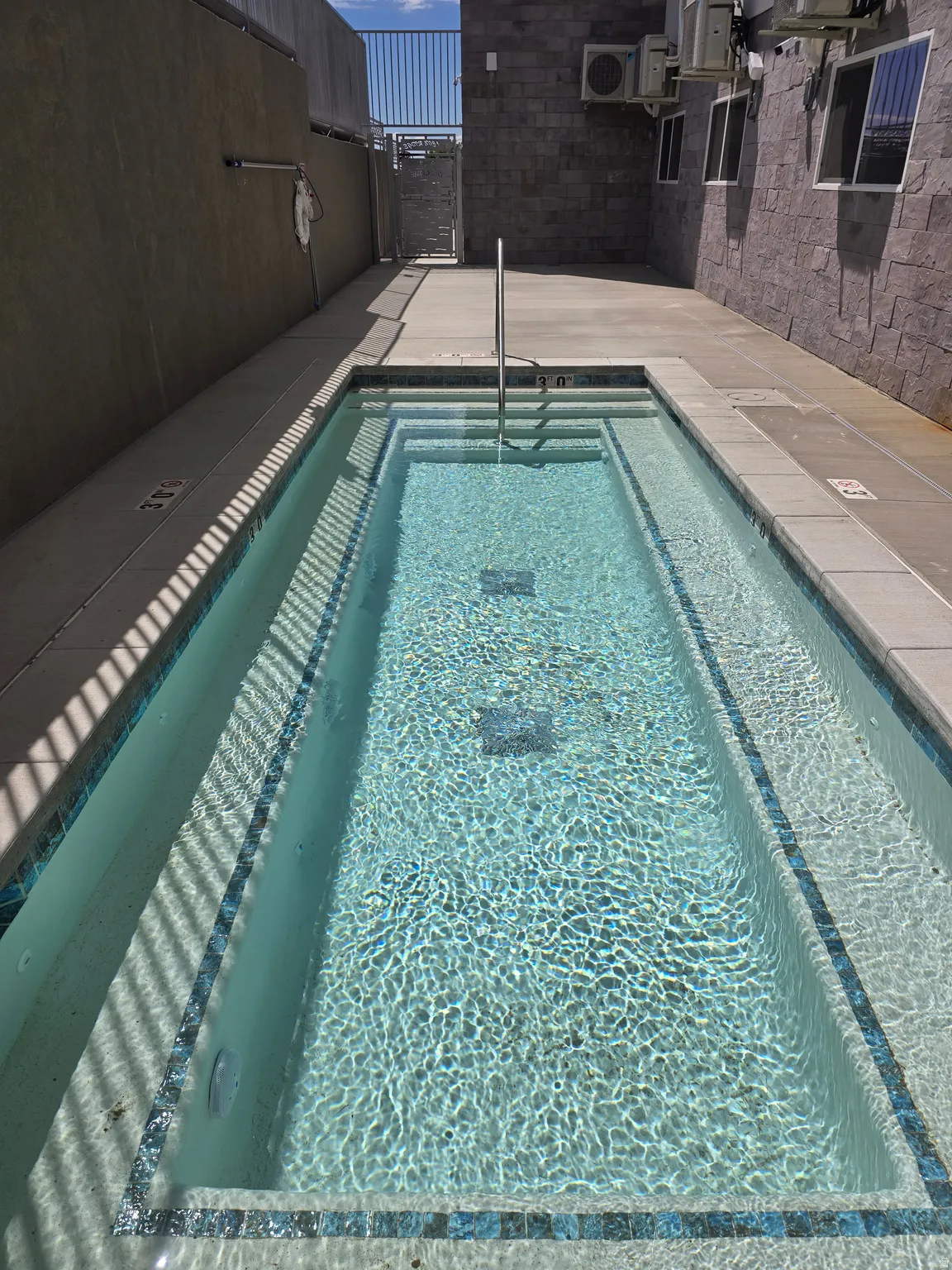 Rectangular wading pool with tiled steps, a stainless steel handrail, and mosaic tile detailing