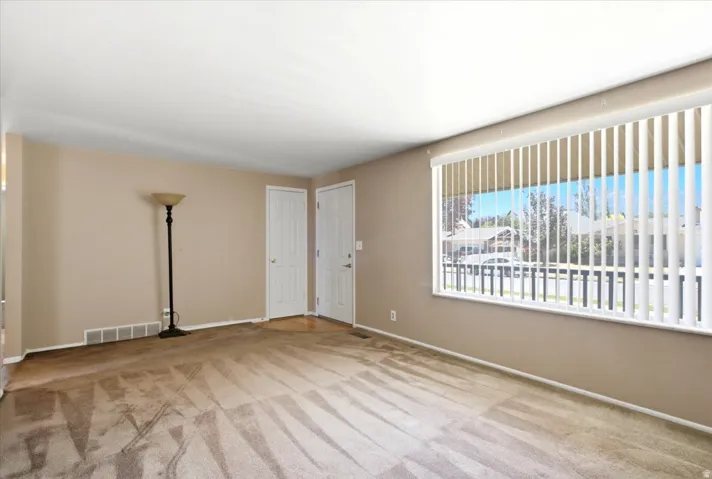 Spacious room featuring neutral-toned walls, carpeted flooring, and a large window with vertical blinds