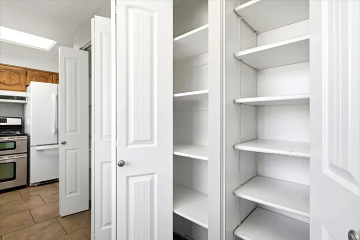 Kitchen pantry featuring multiple adjustable shelves, paneled bifold doors, and a tile floor